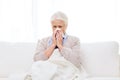 Sick senior woman blowing nose to paper napkin