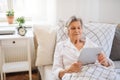 Sick senior woman with headphones and tablet lying in bed at home or in hospital. Royalty Free Stock Photo