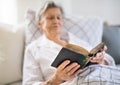 Sick senior woman reading bible book in bed at home or in hospital. Royalty Free Stock Photo