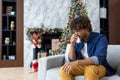 Sick sneezing man with runny nose sitting on sofa at home, hispanic winter day near Christmas tree, cold and allergy in Royalty Free Stock Photo