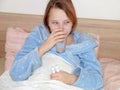 Sick teenage girl drinks pills with water while lying in bed Royalty Free Stock Photo