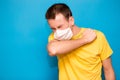 Sick tired man wearing medical mask and coughs into elbow on blue background. Coronavirus, Covid-19, illness person, sore