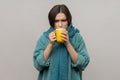 Sick unhealthy woman in scarf holding in hands cup with hot tea feeling chills, drinks hot beverage Royalty Free Stock Photo