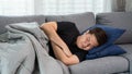 Sick and unwell Asian men holding his head, having a strong headache and sleeping on sofa at home wrapped in grey blanket Royalty Free Stock Photo