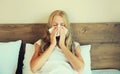 Sick upset woman sneezing blow nose using tissue lying in bed at home