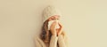 Sick upset woman sneezing blow nose using tissue wearing warm soft knitted clothes, hat and sweater on beige studio background Royalty Free Stock Photo