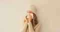 Sick upset woman sneezing blow nose using tissue wearing warm soft knitted clothes, hat and sweater on beige studio background Royalty Free Stock Photo