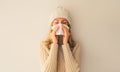 Sick upset woman sneezing blow nose using tissue wearing warm soft knitted clothes, hat and sweater on beige studio background Royalty Free Stock Photo