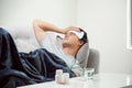 Sick wasted man lying in sofa suffering cold and winter flu virus having medicine tablets in health care concept looking