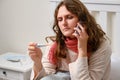 Sick woman calls the doctor on the phone with a thermometer in her h