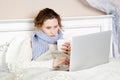 Sick woman feeling bad, resting and working with her laptop and internet in her bed at home Royalty Free Stock Photo