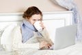 Sick woman feeling bad, resting and working with her laptop and internet in her bed at home Royalty Free Stock Photo