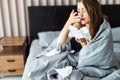 Sick woman froze and caught a cold from an unheated flat covered with warm blanket sit in bed drinking cup with hot beverage or Royalty Free Stock Photo