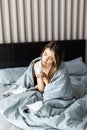 Sick woman froze and caught a cold from an unheated flat covered with warm blanket sit in bed drinking cup with hot beverage or Royalty Free Stock Photo