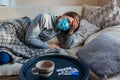 Sick woman having flu or cold. Girl lying in bed wearing protective mask by pills and water on table Royalty Free Stock Photo