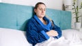 Portrait of sick woman lying in bed and measuring temperature with digital thermometer Royalty Free Stock Photo