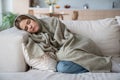 Sick woman lying on sofa with eyes closed wrapped in plaid of shiver, cold, flu, virus, inflammation