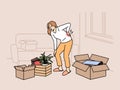 Sick woman moving to new apartment and suffers from back pain, stands among heavy boxes