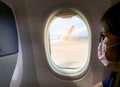 Sick woman passenger wear face mask and eyeglasses sit on passenger economy seat near cabin window inside airplane. Passenger