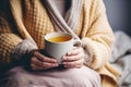 A sick woman is sitting on the bed with a mug of hot drink.