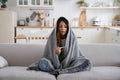 Sick woman sitting on sofa covered blanket looking at electronic thermometer measuring temperature Royalty Free Stock Photo