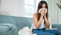 Sick woman sitting under blanket on sofa and sneeze with tissue paper in living room Royalty Free Stock Photo