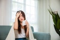 Sick woman sitting under blanket on sofa and sneeze with tissue paper in living room Royalty Free Stock Photo