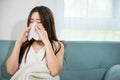 Sick woman sitting under blanket on sofa and sneeze with tissue paper in living Royalty Free Stock Photo