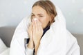 Sick woman sneezing holding tissue paper napkin sitting on couch at home Royalty Free Stock Photo