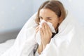 Sick woman sneezing holding tissue paper napkin sitting on couch at home Royalty Free Stock Photo