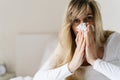 Sick woman suffering from running stuffy nose and sore throat. Upset ill european lady sits in bed, blowing her nose using paper Royalty Free Stock Photo