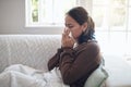 Sick woman, tissue and blowing nose with sinus, flu or illness on living room sofa at home. Young female person with