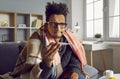 Sick young african american man checking his temperature wrapped in a blanket at home. Royalty Free Stock Photo