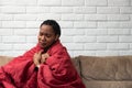 Sick young african woman feeling cold covered with blanket sit on sofa, ill black girl shivering freezing warming at home wrapped Royalty Free Stock Photo