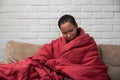 Sick young african woman feeling cold covered with blanket sit on sofa, ill black girl shivering freezing warming at home wrapped Royalty Free Stock Photo