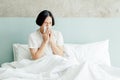 Sick young Asian man blowing his nose while sitting on bed at home Royalty Free Stock Photo