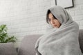Sick young asian woman sit on sofa at home wrapped covered in warm duvet or blanket, She feeling unhealthy ill Royalty Free Stock Photo