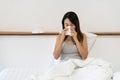 Sick young Asian woman sitting on bed blowing her nose on a tissue conceptual of healthcare , seasonal flu, rhinitis or an Royalty Free Stock Photo