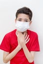 Sick young boy clutches his throat with face mask on. Royalty Free Stock Photo