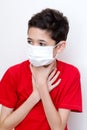 Sick young boy clutches his throat with face mask on.