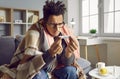 Sick young indian man checking his temperature wrapped in a blanket at home. Royalty Free Stock Photo