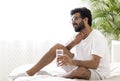Sick indian man suffering throat ache while sitting on bed at home Royalty Free Stock Photo