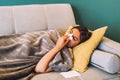 Sick young woman blowing her nose using facial tissues while lying on the sofa Royalty Free Stock Photo
