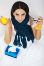 Sick young woman at home on the sofa, she is covering with a blanket, taking temperature and blowing her nose with a tissue Royalty Free Stock Photo