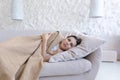 Sick young woman lying on a pillow on the couch at home, covered with a brown blanket Royalty Free Stock Photo