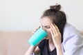 Sick young woman sits at home with a severe headache and drinks pills with water