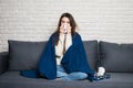 Sick young woman sitting on sofa blowing her nose at home Royalty Free Stock Photo