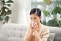 Sick young woman sitting on sofa blowing her nose at home in the sitting room. Photo of sneezing woman in paper tissue Royalty Free Stock Photo