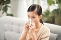 Sick young woman sitting on sofa blowing her nose at home in the sitting room. Photo of sneezing woman in paper tissue Royalty Free Stock Photo