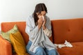 Sick young woman wrapped in blanket at home, blowing her nose with tissue Royalty Free Stock Photo